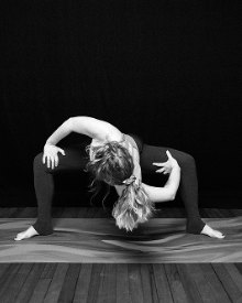 Black and white photo of Morgane in a yoga pose on a mat, arms wrapped around her bent leg.